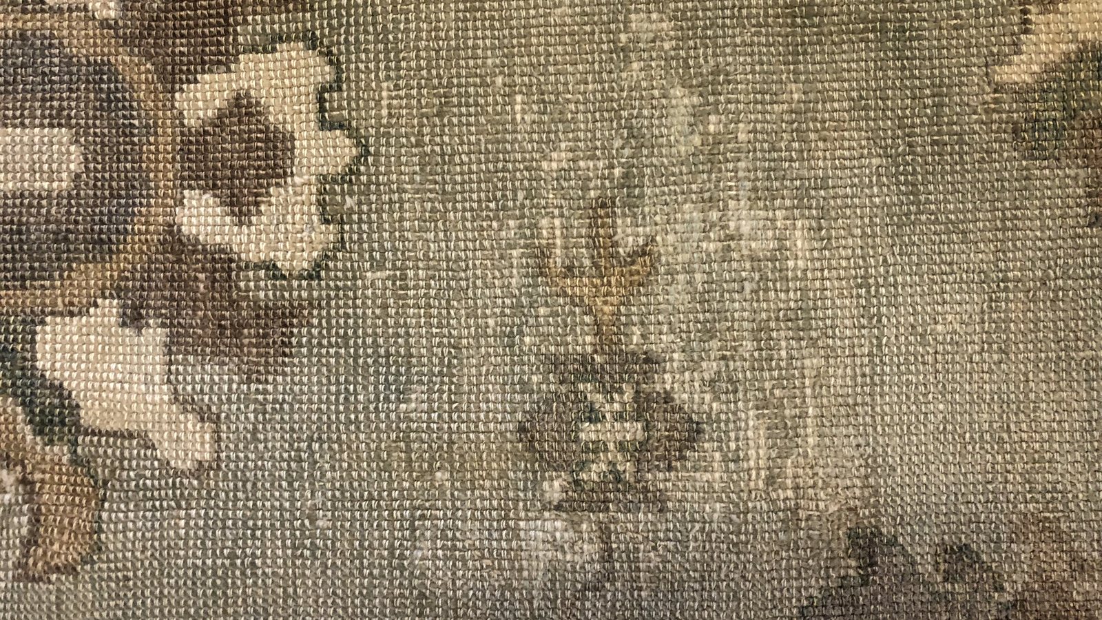 The reverse of a wool rug under inspection lighting, where clay and old repairs show before the pile gives them away